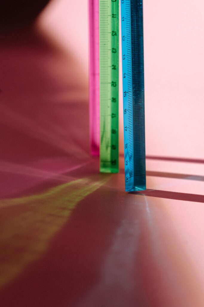 Close-up of vibrant rulers casting shadows on a pink surface.